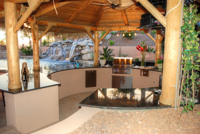 Custom palapa-covered outdoor kitchen with a stone waterfall and pool built by All Terrain in Tucson