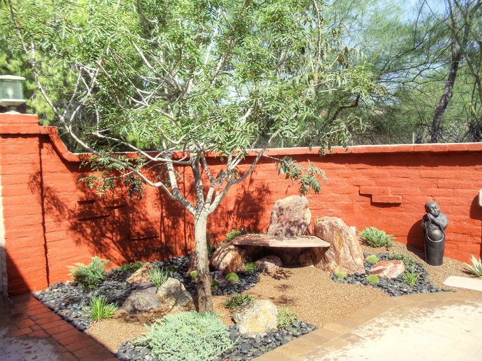 Zen-style courtyard landscape with boulders, desert plantings, and a red stucco wall
